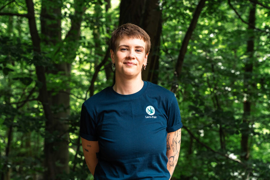 Junge Frau in Lern-Fair T-Shirt vor Wald 
