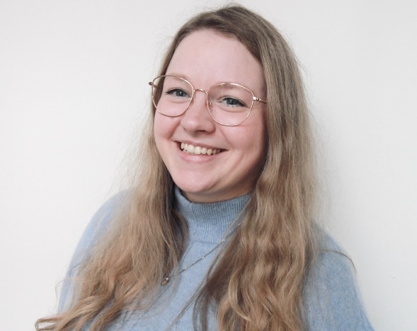 Junge Frau in Lern-Fair T-Shirt vor Wald mit Eulen Maskottchen