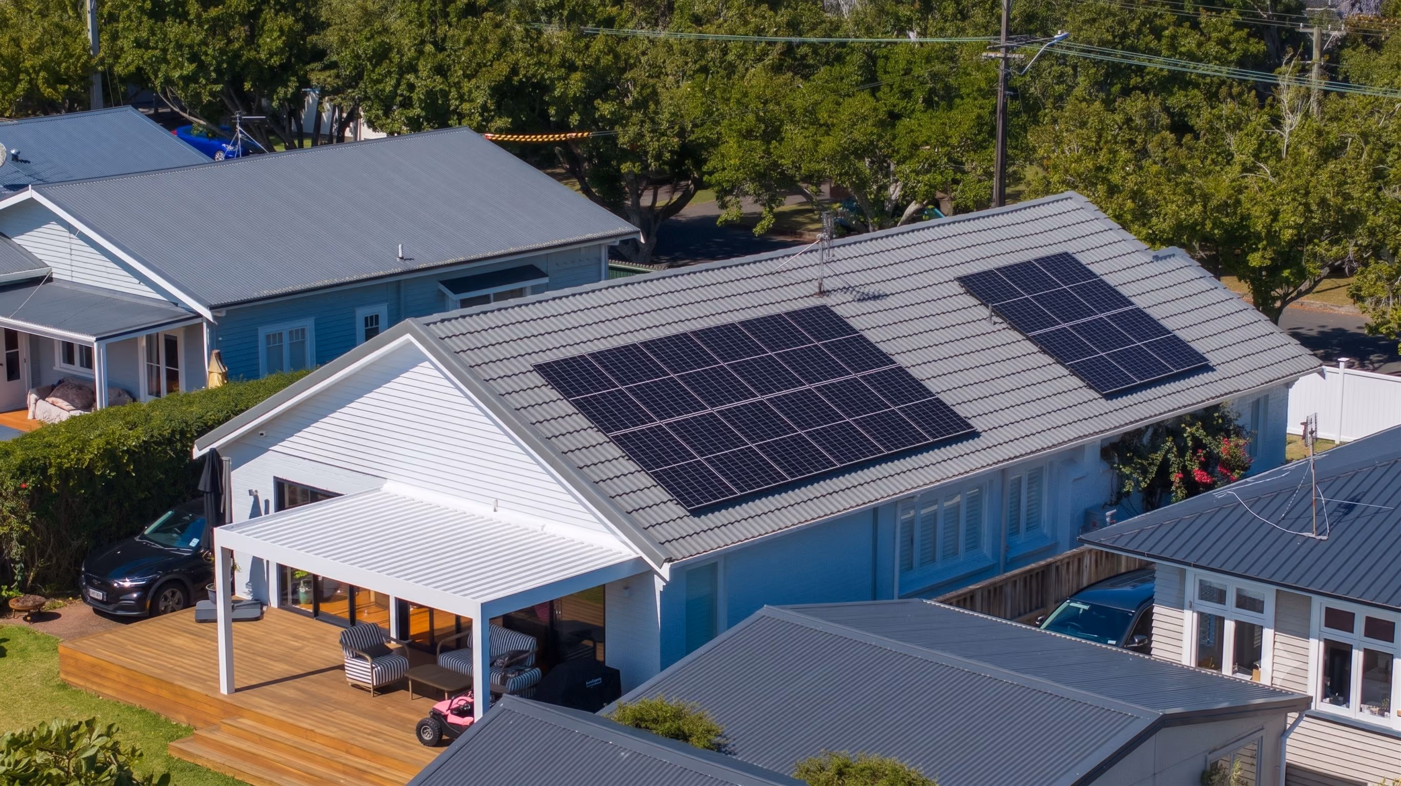 White house with solar panels on gray tiled roof and wooden deck with chairs and table.