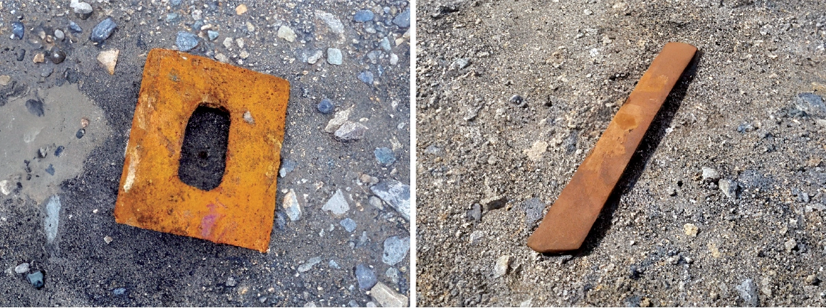 Two rusted steel debris pieces, including a flat plate and a bar, lying on rocky gravel at the mine site, used as buried ferrous detection targets.