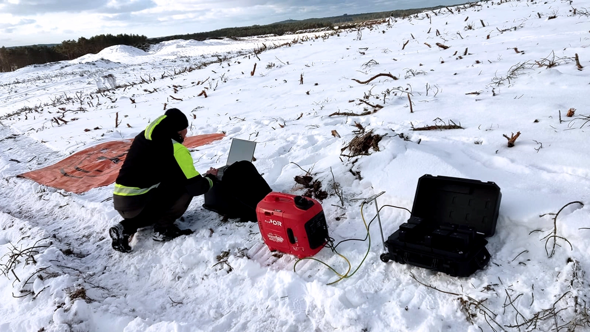 Explosive.pl operator reviewing drone magnetometer survey data on laptop in snow-covered terrain at the northern Poland UXO survey site with portable generator and battery charging station