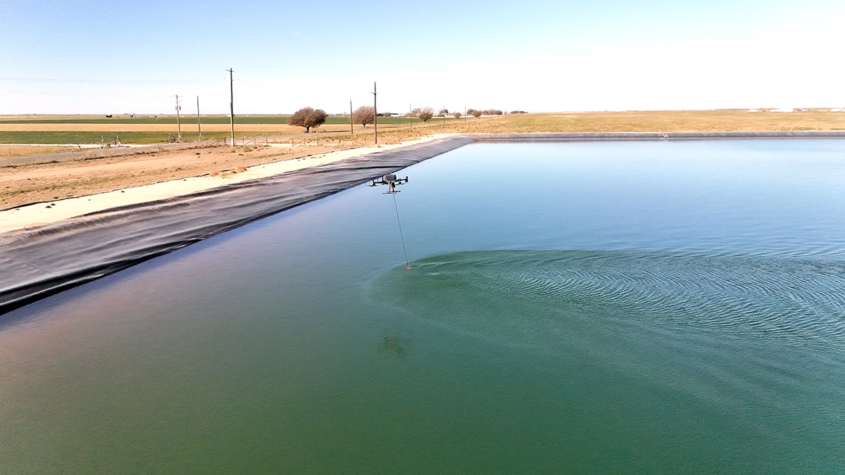 DJI M300 drone carrying an echo sounder over a lined frac pond during a bathymetric survey in West Texas.