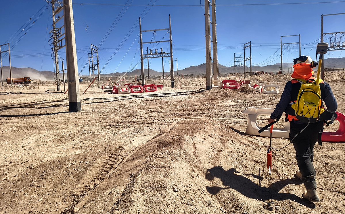 Surveyor carrying field equipment among electrical infrastructure at a Chilean mine