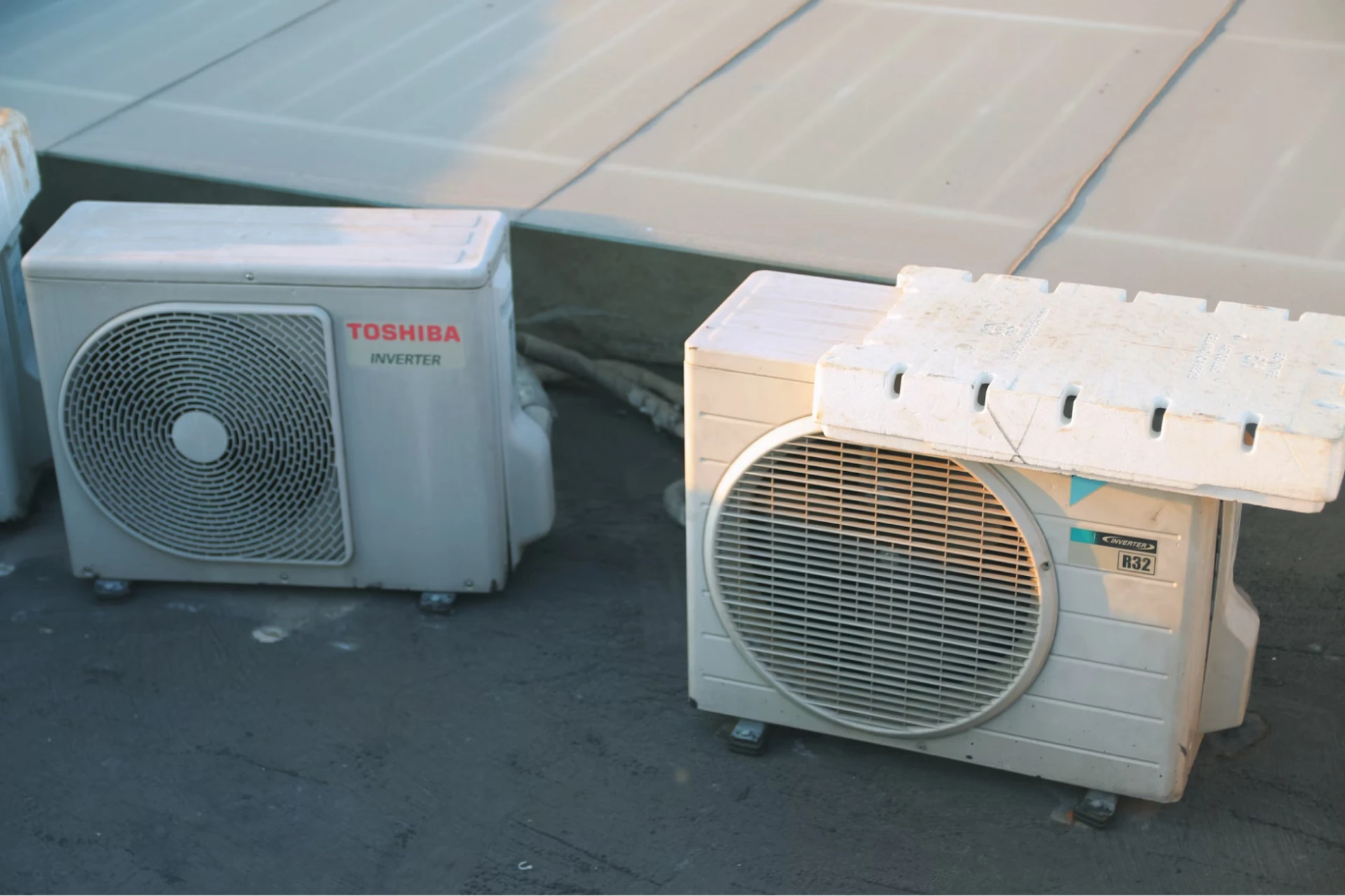 Two heat pumps sit next to each other on a concrete surface. 