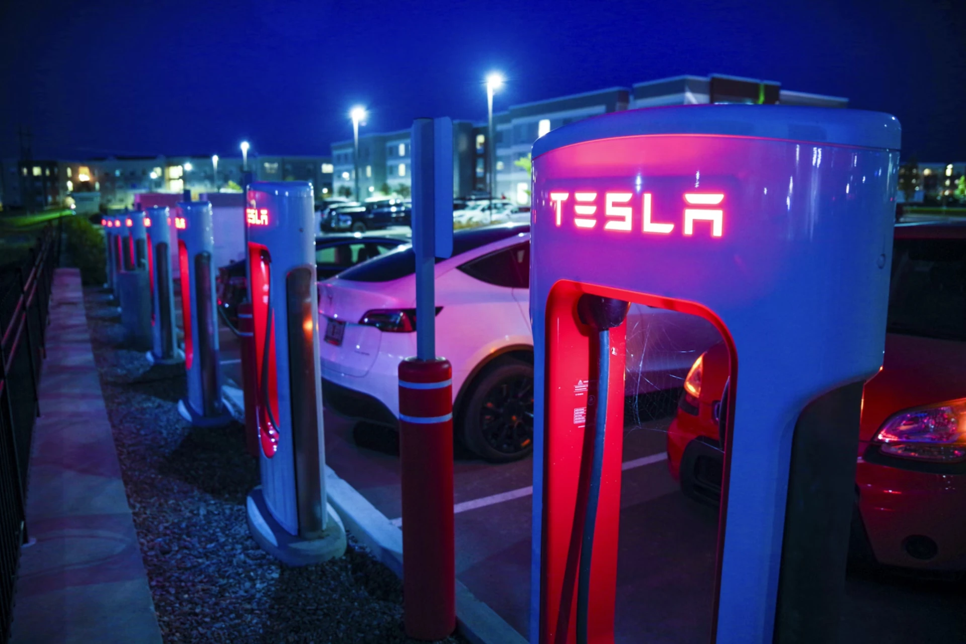  A row of Tesla charge points and Tesla cars at a well-lit, nighttime parking lot.