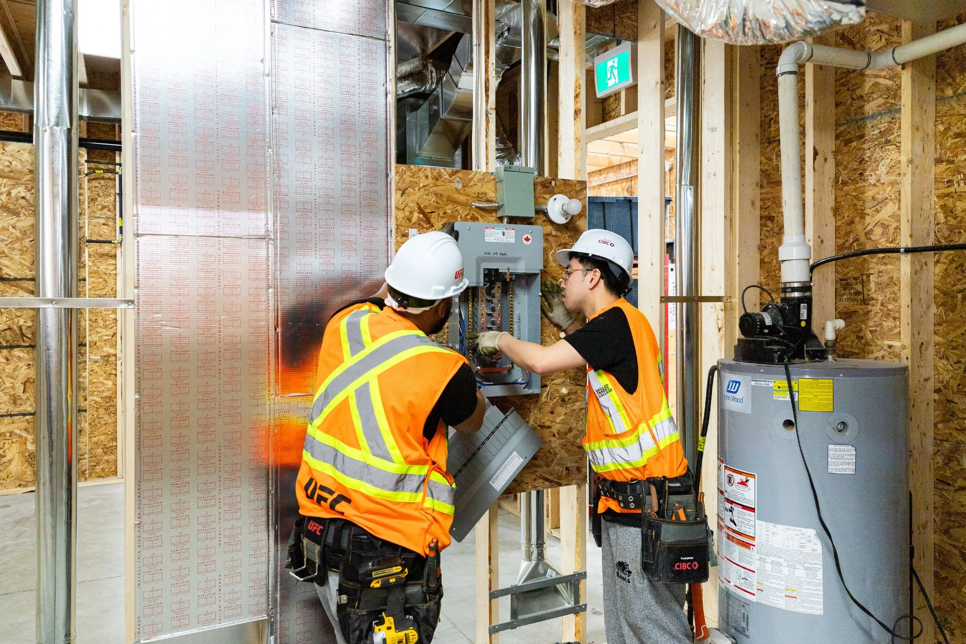 Two people in hard hats working on an electrical system