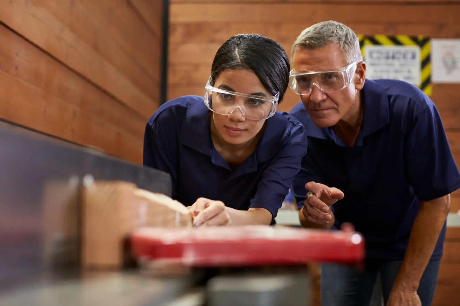 An older male carpenter teaching a female apprentice