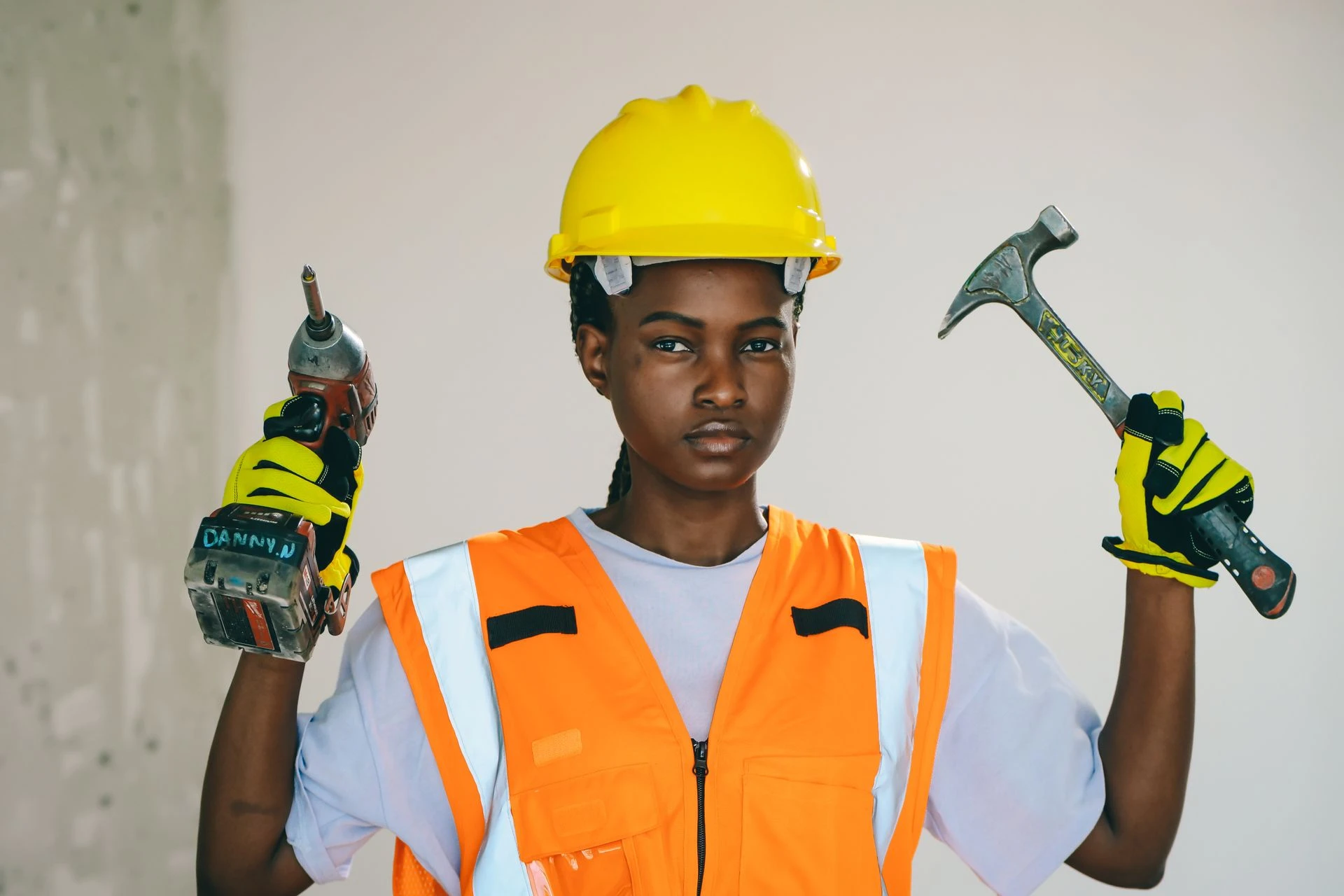 a woman construction worker in safety gear holding a drill and hammer