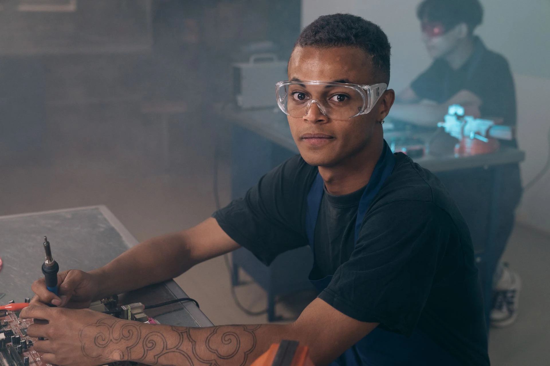 A young man wearing safety glasses using a soldering iron in a workshop learning environment
