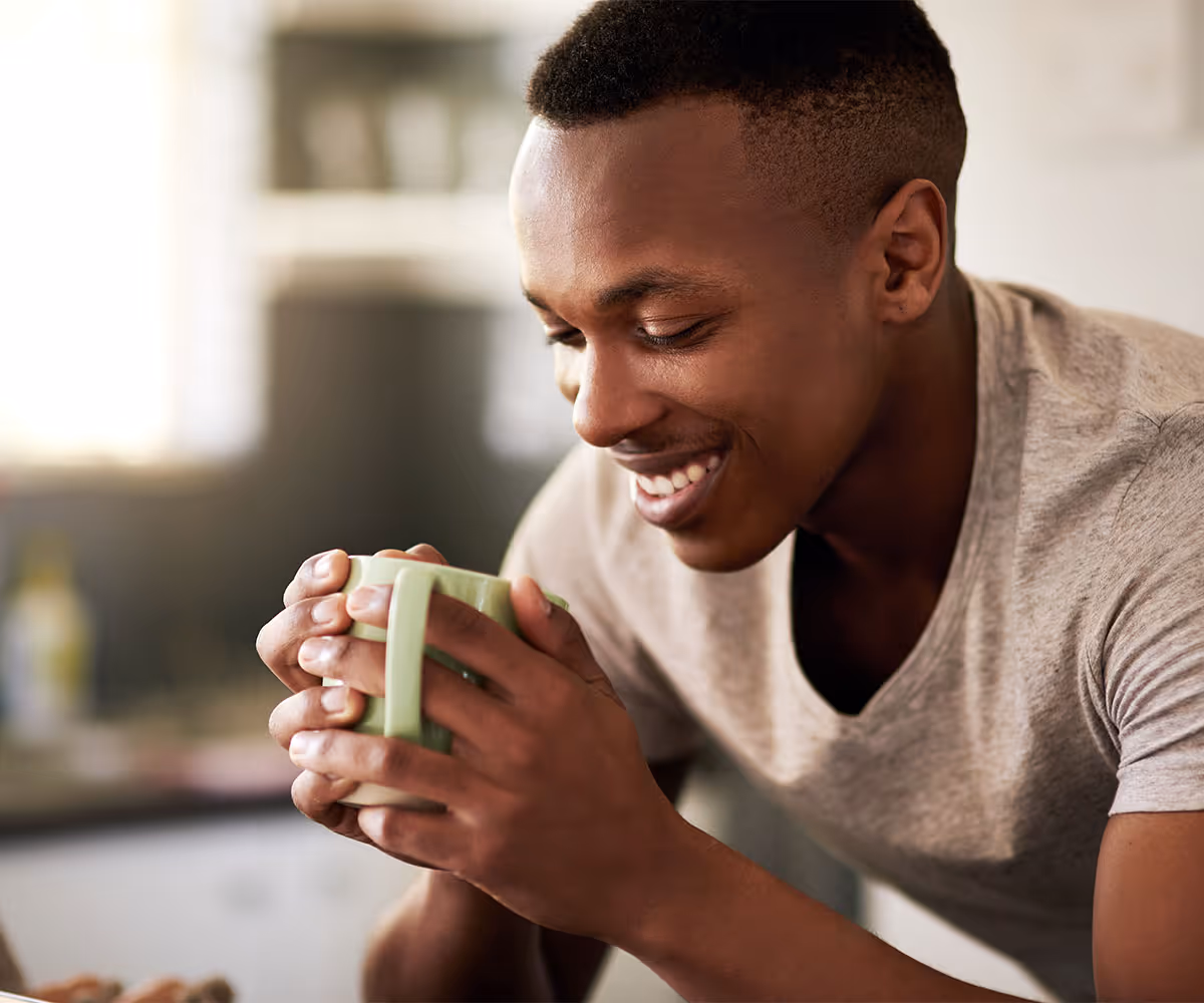 A person smiling into a mug of warm coffee.