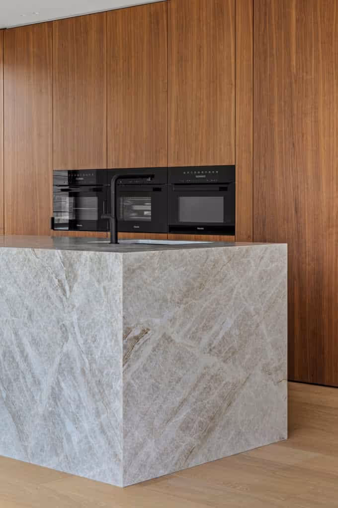Professionele vastgoedfotografie van een groot, marmeren kookeiland met houten kastenwand.