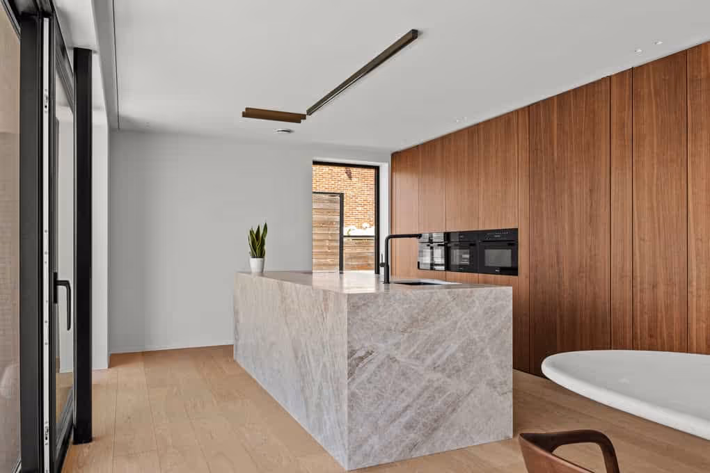 Luxe interieurfotografie van een warme keuken met houten kasten, marmeren kookeiland en sfeervolle verlichting.