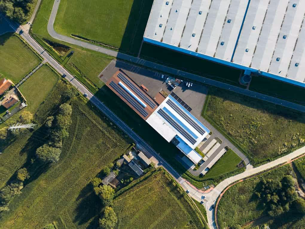 Industriële dronefoto van een groot wit fabriekspand met plat dak en omliggend groen in Beringen.