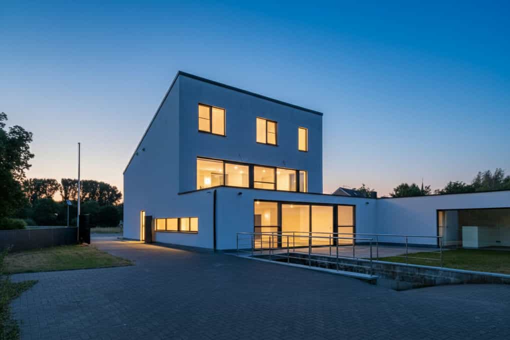 Virtuele schemering vastgoedfoto van een moderne, witte villa met verlichte interieurs in Hasselt.