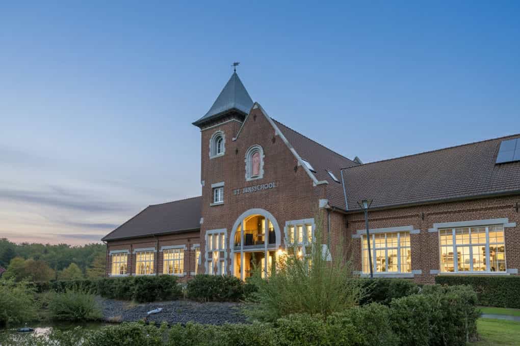 Vastgoedfoto avondsfeer van een witte boerderijwoning met zwarte elementen en grote tuin in Genk.