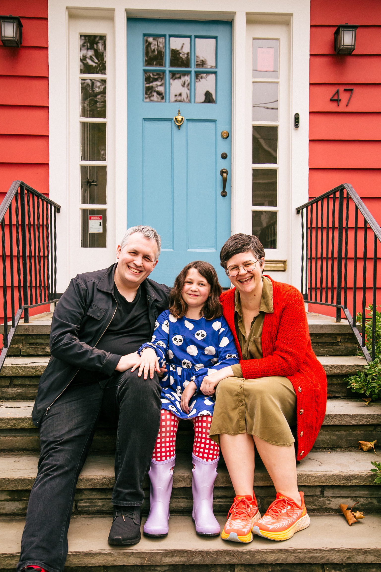 An adorable family of 3 sitting in front of a red house