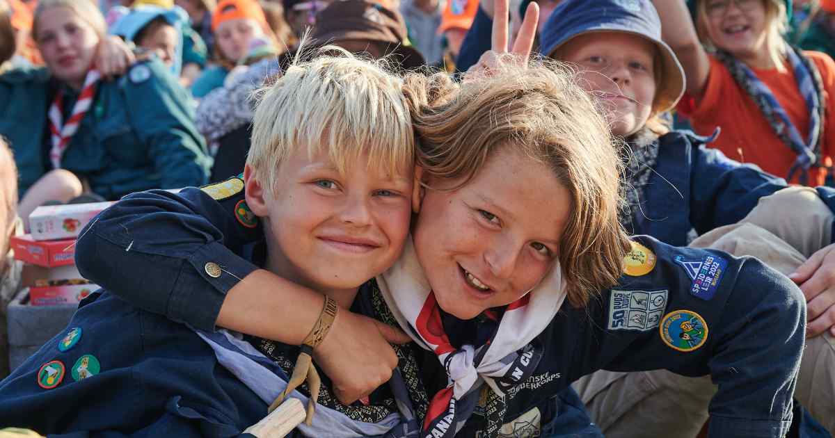 to spejdere ser ind i kameraet imens de smiler og holder hinanden om skuldrene