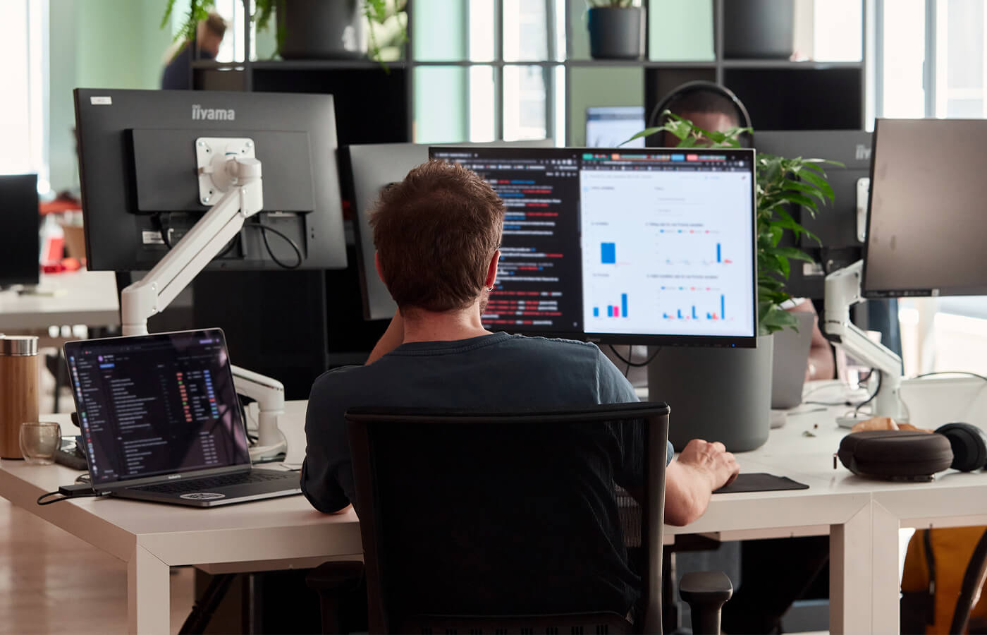 Man working at a desk with multiple monitors displaying code and data charts in a modern office.