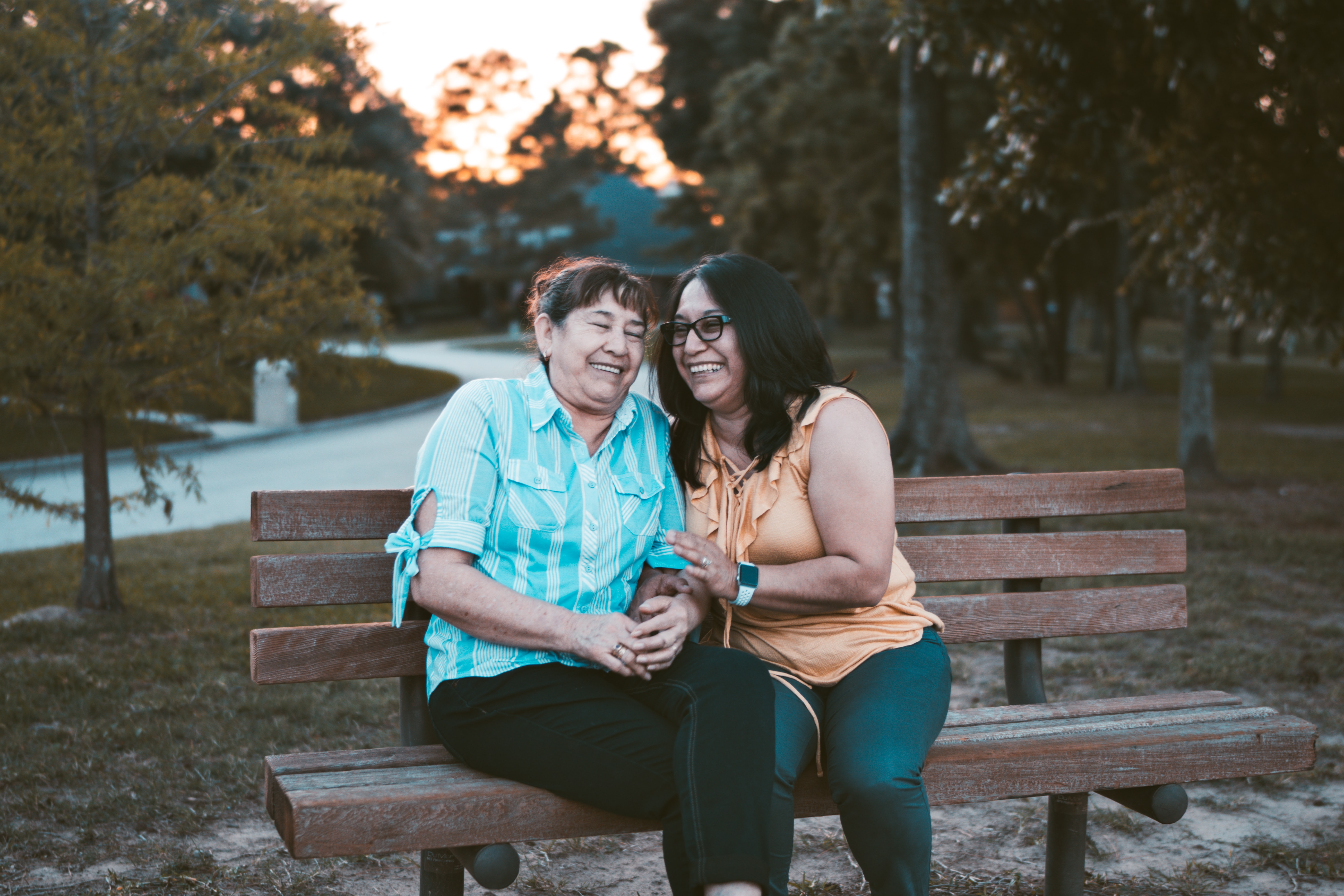 A picture of two women laughing on the park bench at sunset.
