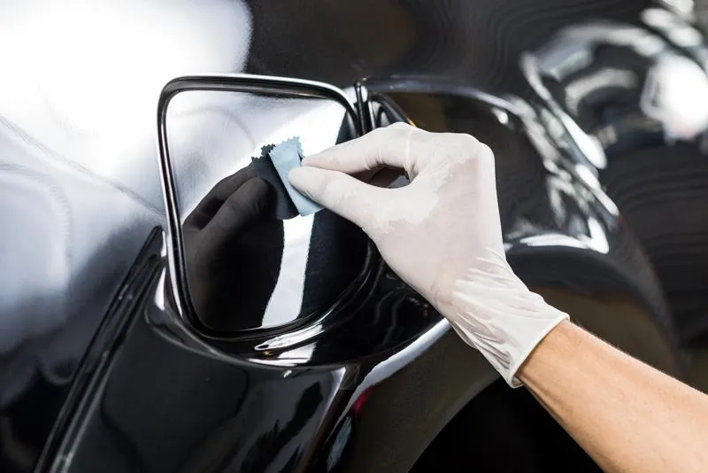 Application d'un traitement céramique sur une voiture noire, réalisée par un professionnel portant des gants pour protéger la carrosserie des rayures et des agressions extérieures.