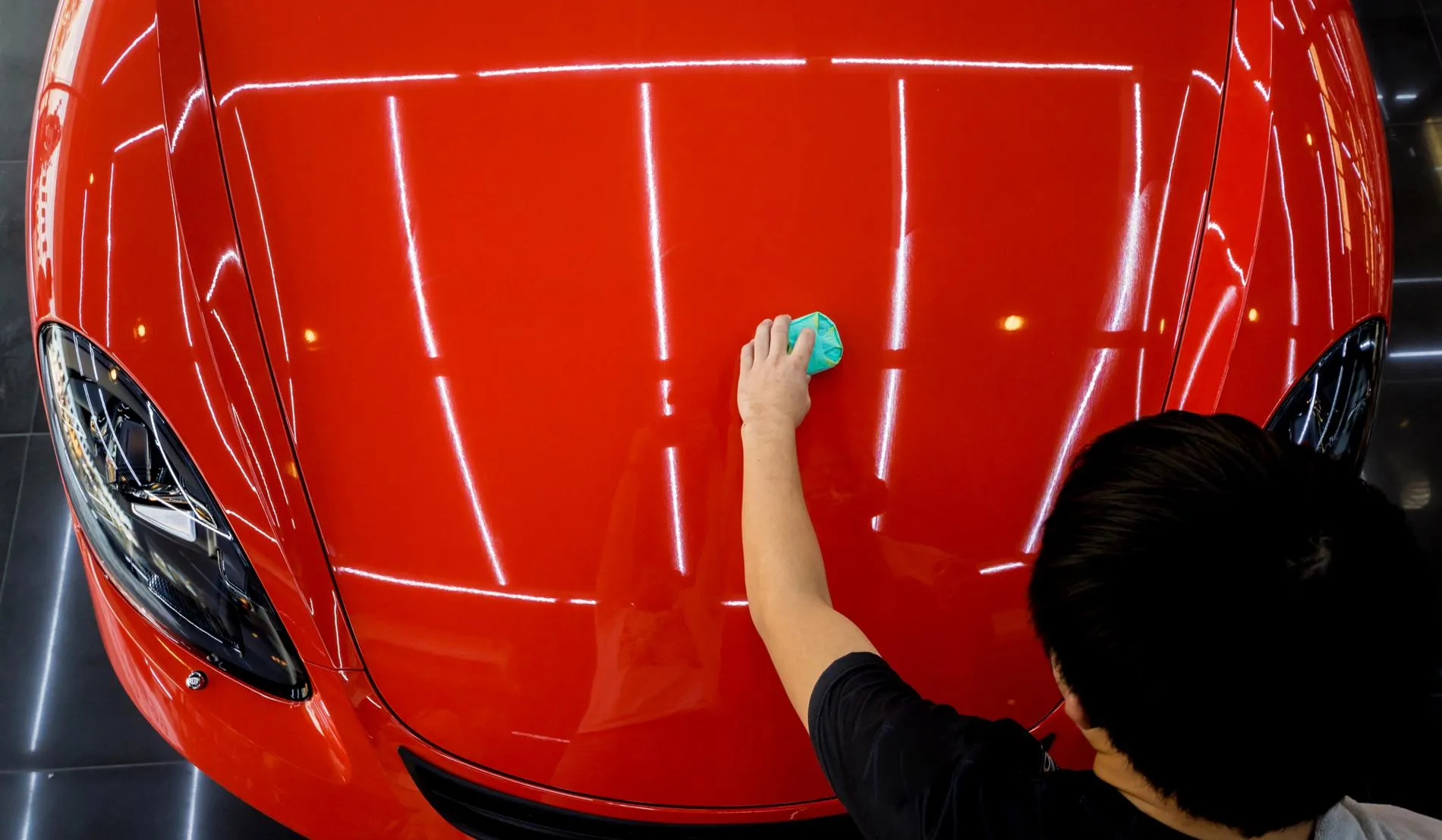 Vue d'en haut d'un professionnel appliquant un traitement de protection sur le capot d'une voiture rouge brillante, mettant en valeur la finition et l'éclat de la carrosserie.