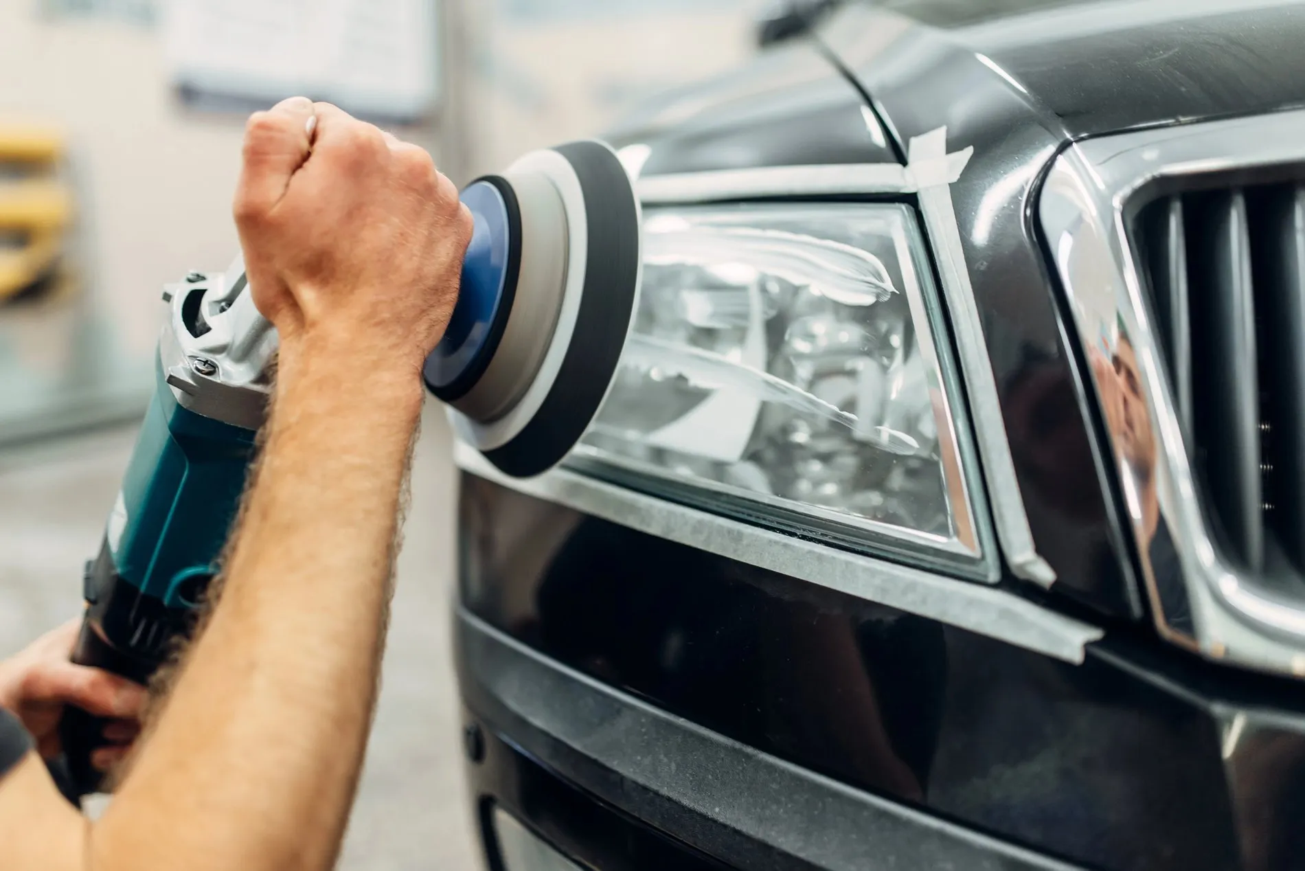 Rénovation d’un phare de voiture avec une polisseuse électrique dans un atelier automobile, montrant un travail précis et méticuleux sur un véhicule noir.