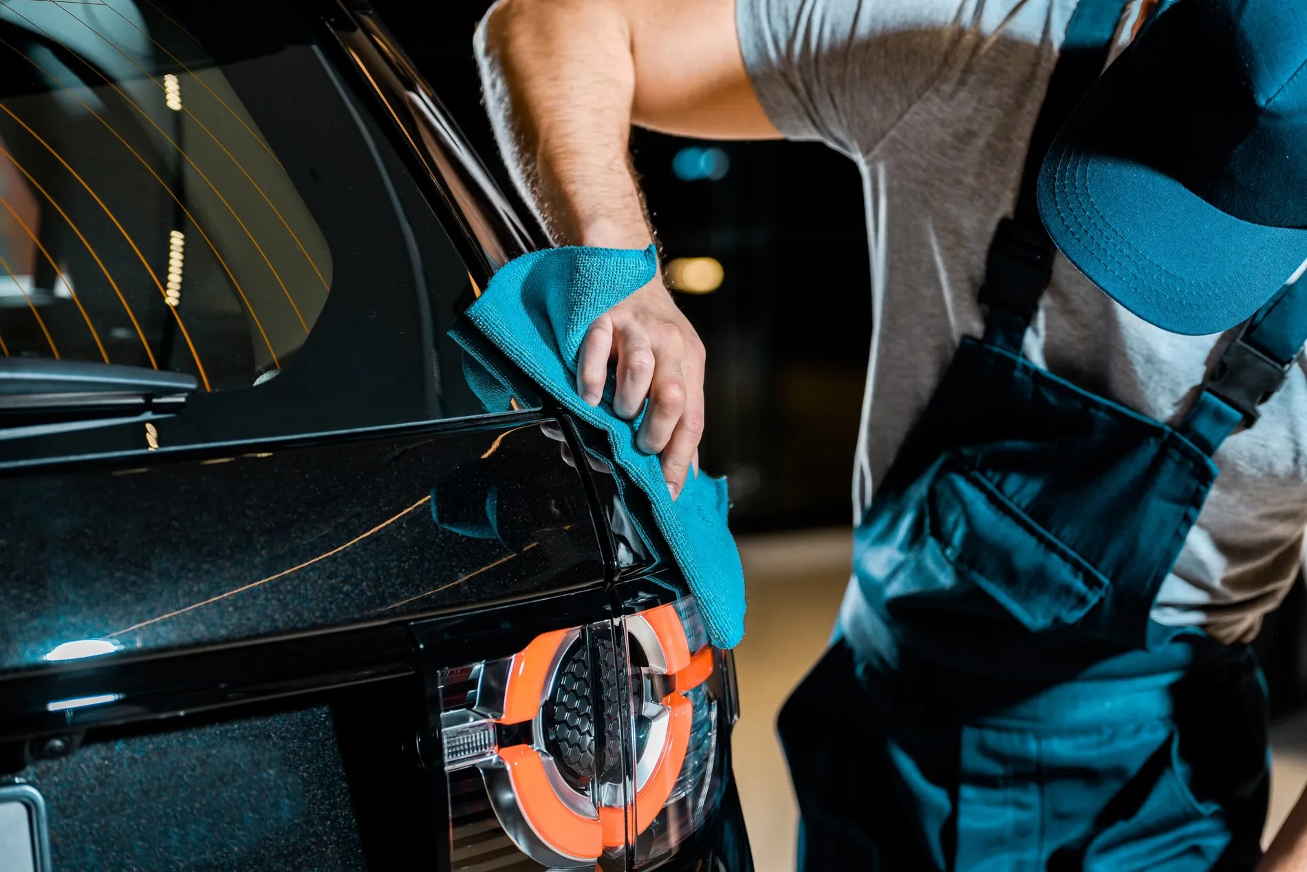 Nettoyage et finition d’une carrosserie de voiture noire avec un chiffon en microfibre, mettant en valeur la brillance de la peinture et les détails des feux arrière.