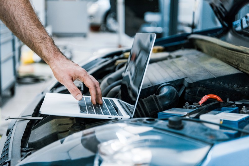 Un mécanicien utilise un ordinateur portable posé sur le moteur ouvert d'une voiture pour effectuer un diagnostic automobile.