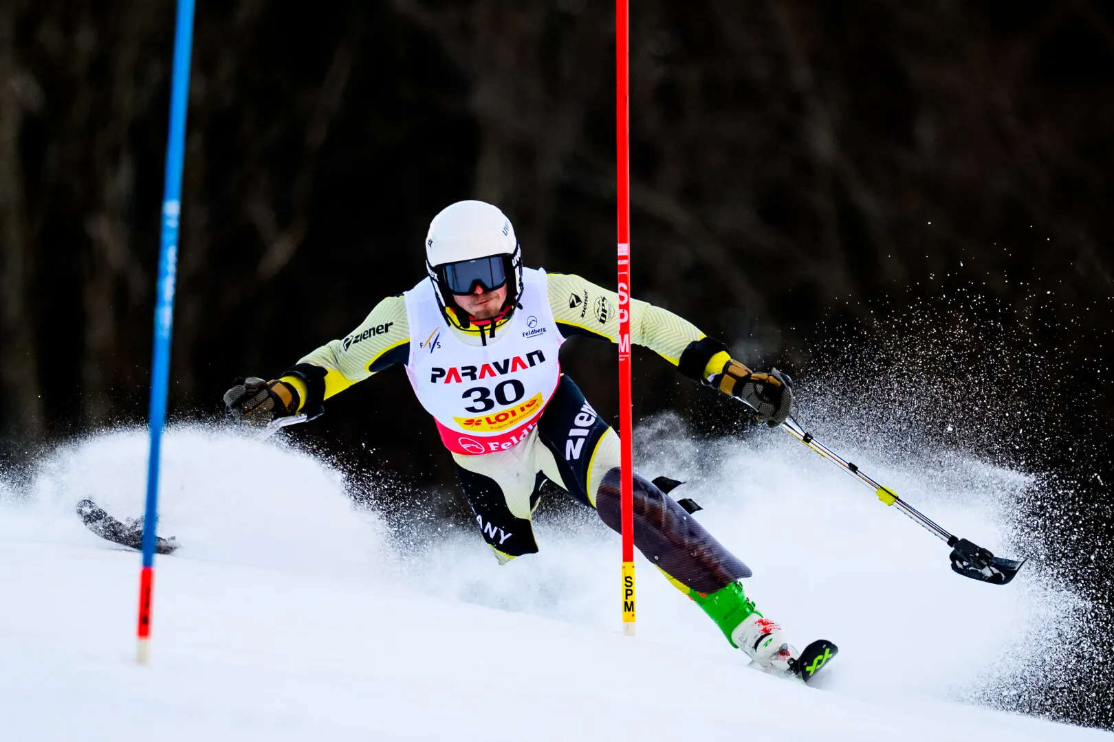 Paralympic alpine skier wearing bib number 30 skis aggressively around a red gate on a snowy slope.