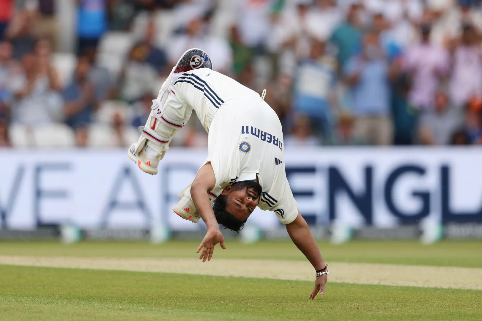 Cricket player in Indian team uniform performing a celebratory front flip on the field.
