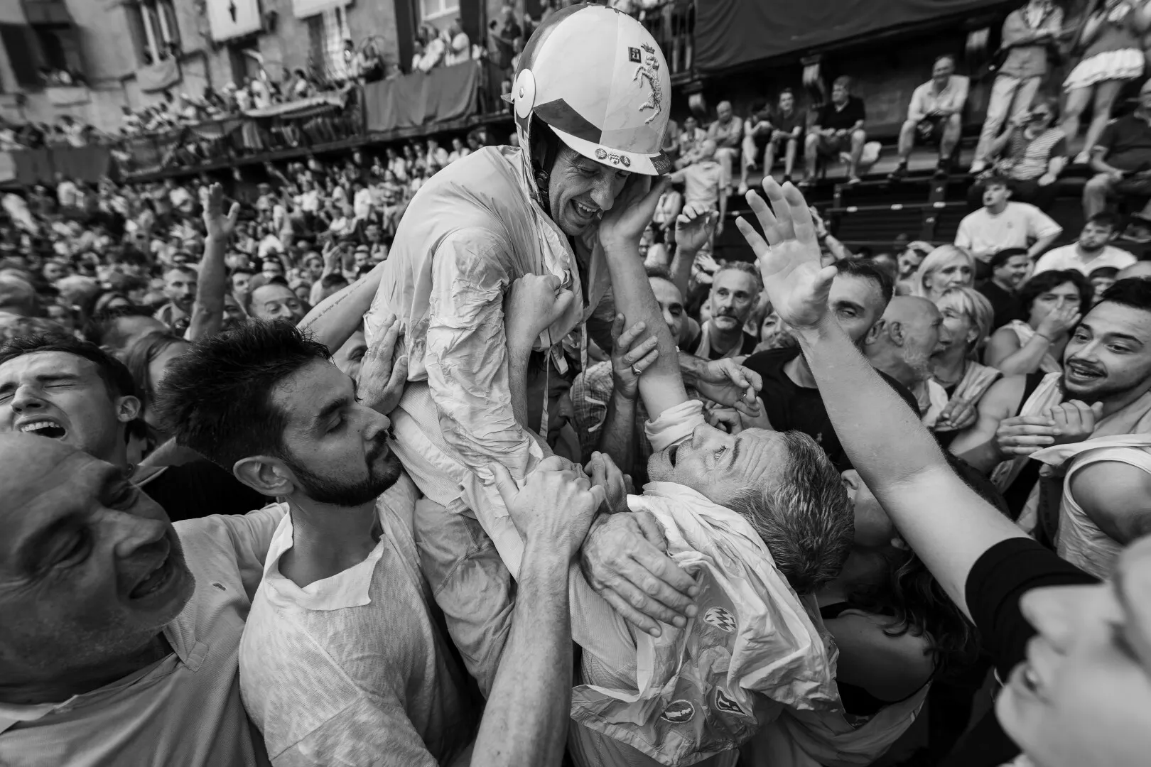 Black and white photo of a crowd lifting a man wearing a helmet and protective gear in celebration.