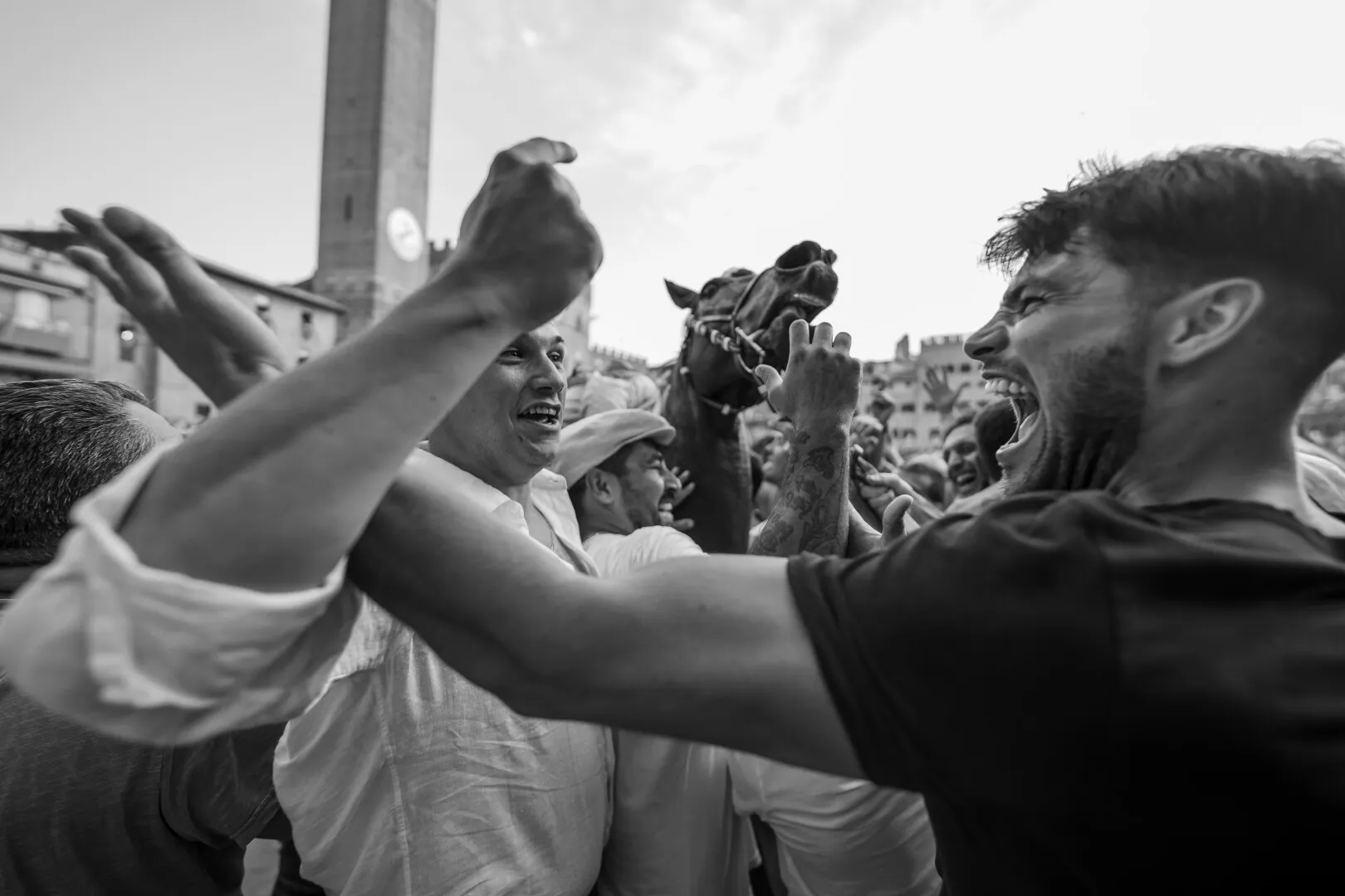 Black and white photo of a crowd of people enthusiastically surrounding and interacting with a horse in an urban square.