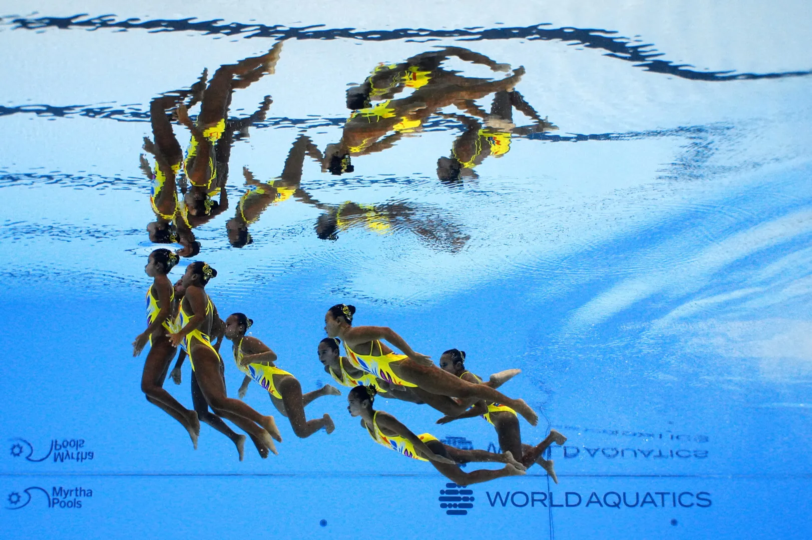 Synchronized swimming team performing underwater in a pool with World Aquatics and Myrtha Pools logos visible.