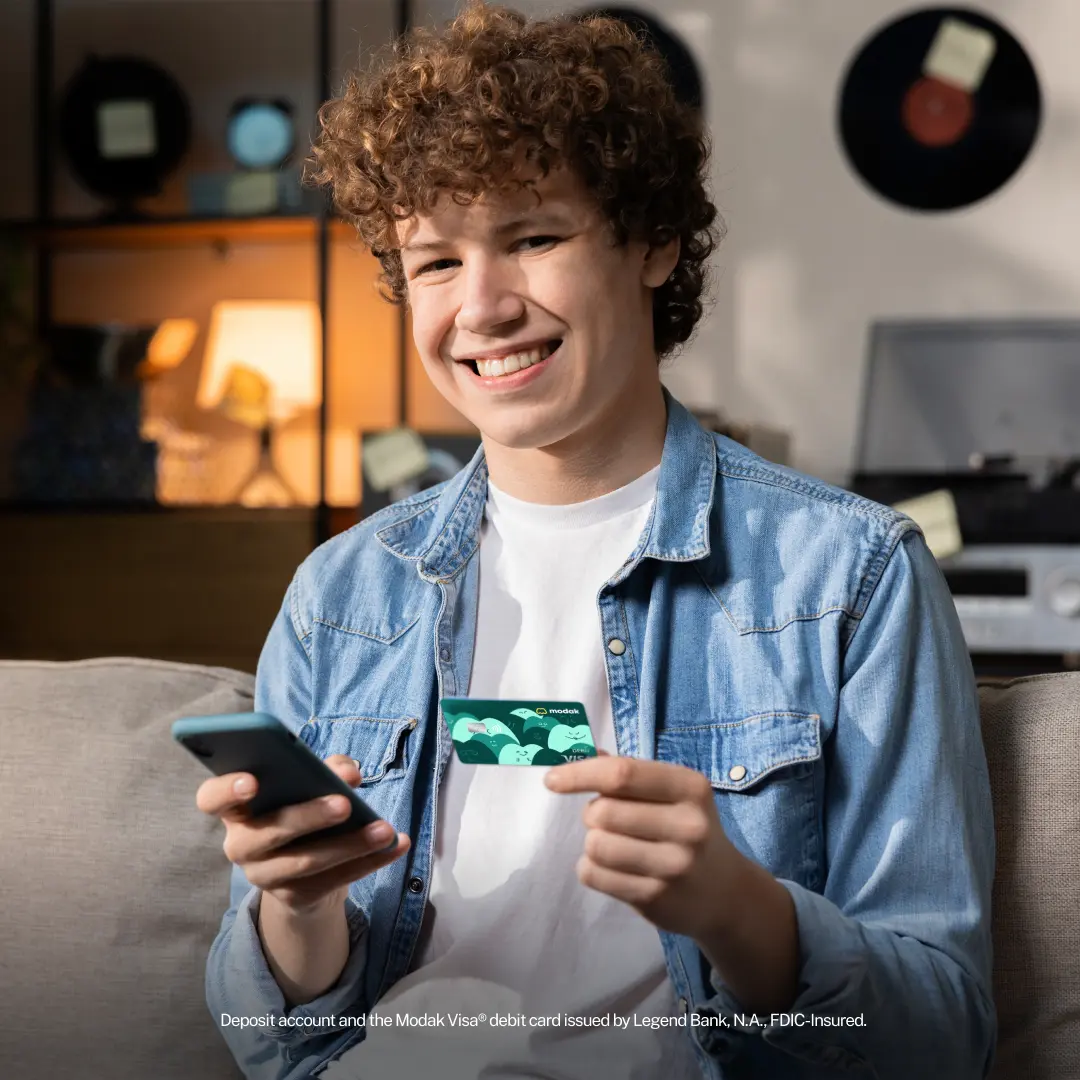 Teen holds Modak Visa debit card while he smiles