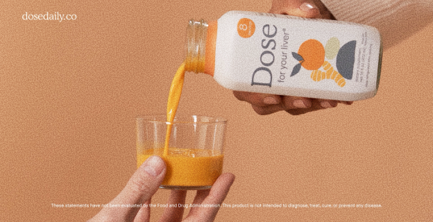Hand pouring orange-colored Dose for your liver juice from a bottle into a glass against a beige background.