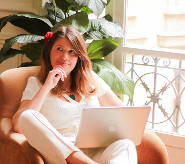 Coach business intuitive accompagnant les solopreneurs atypiques et visionnaires, assise avec un air de stratège avec un mac sur les genoux 