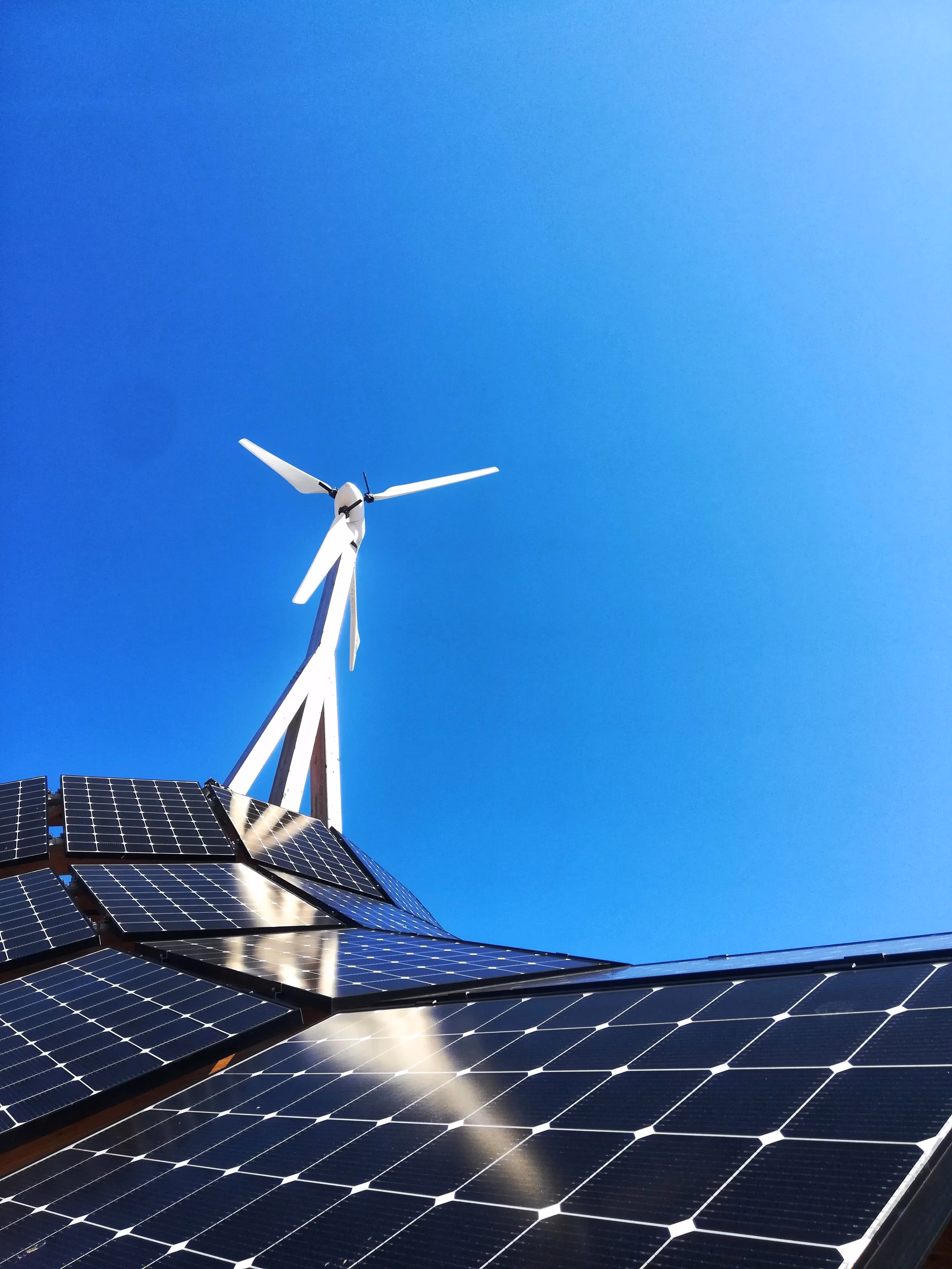 A wind turbine on top of solar panels against a blue sky.