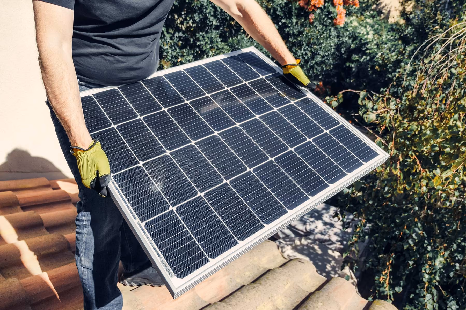 A man holding a solar panel on a rooftop.