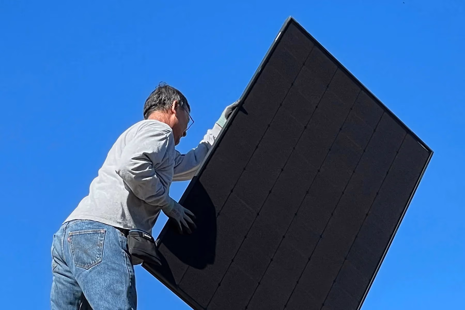A man installing a solar panel on top of a roof.