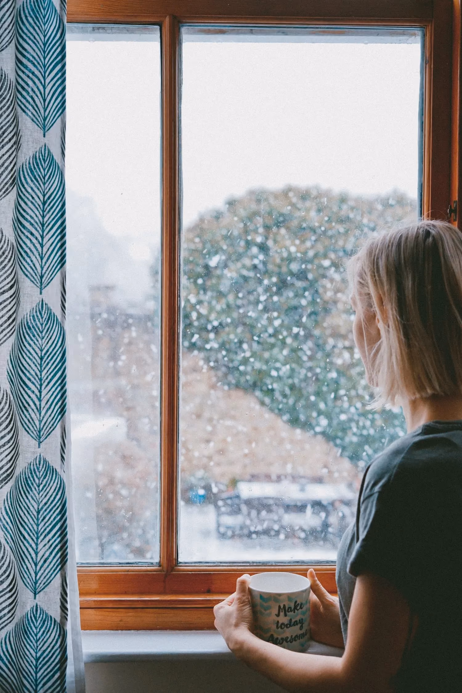 A woman looking out a window with a cup of coffee.