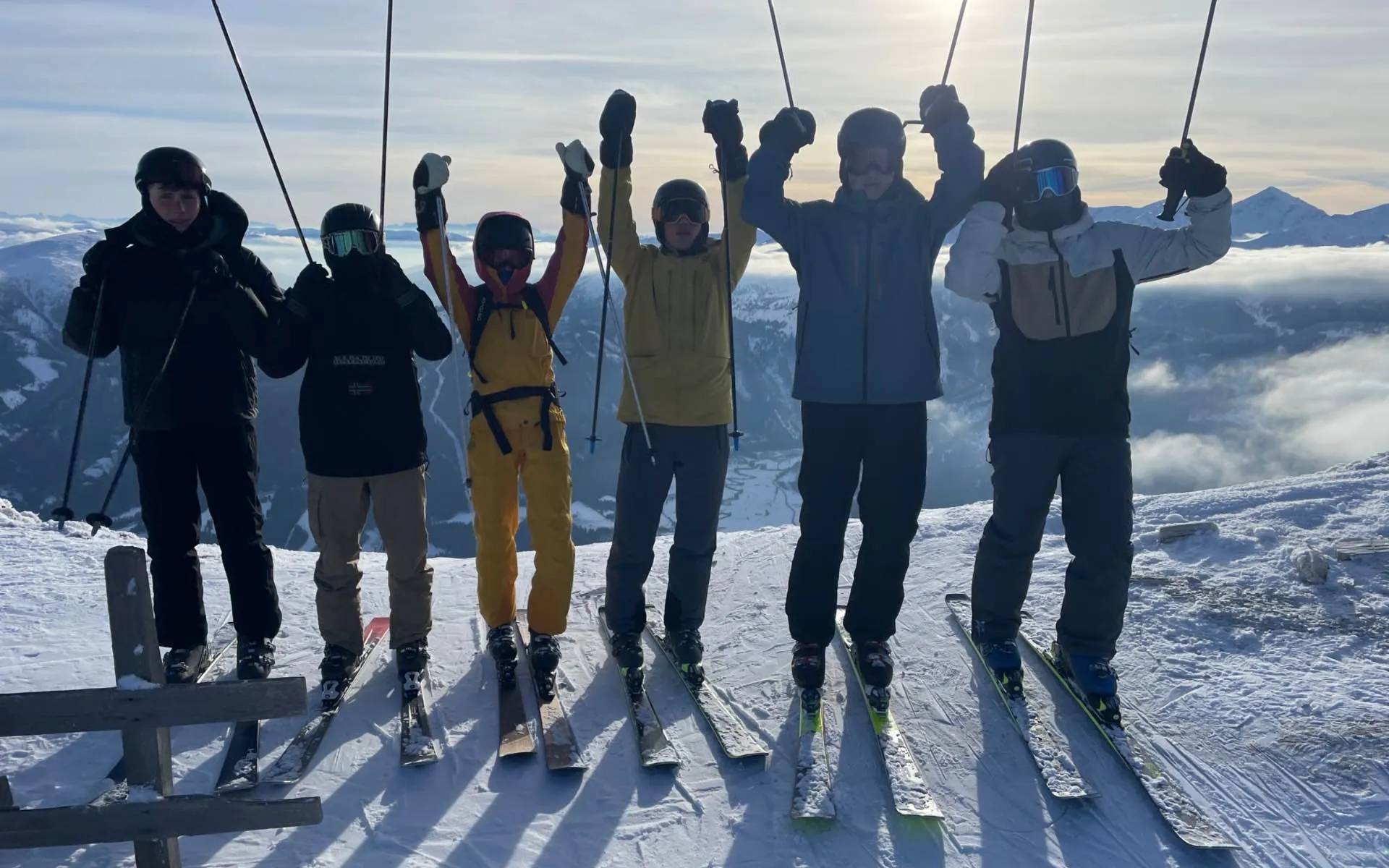 Die Teilnehmer stehen in ihren Skianzügen und Skiern vor schneebedeckten Bergen und werfen ihre Skistöcke und Hände in die Luft.