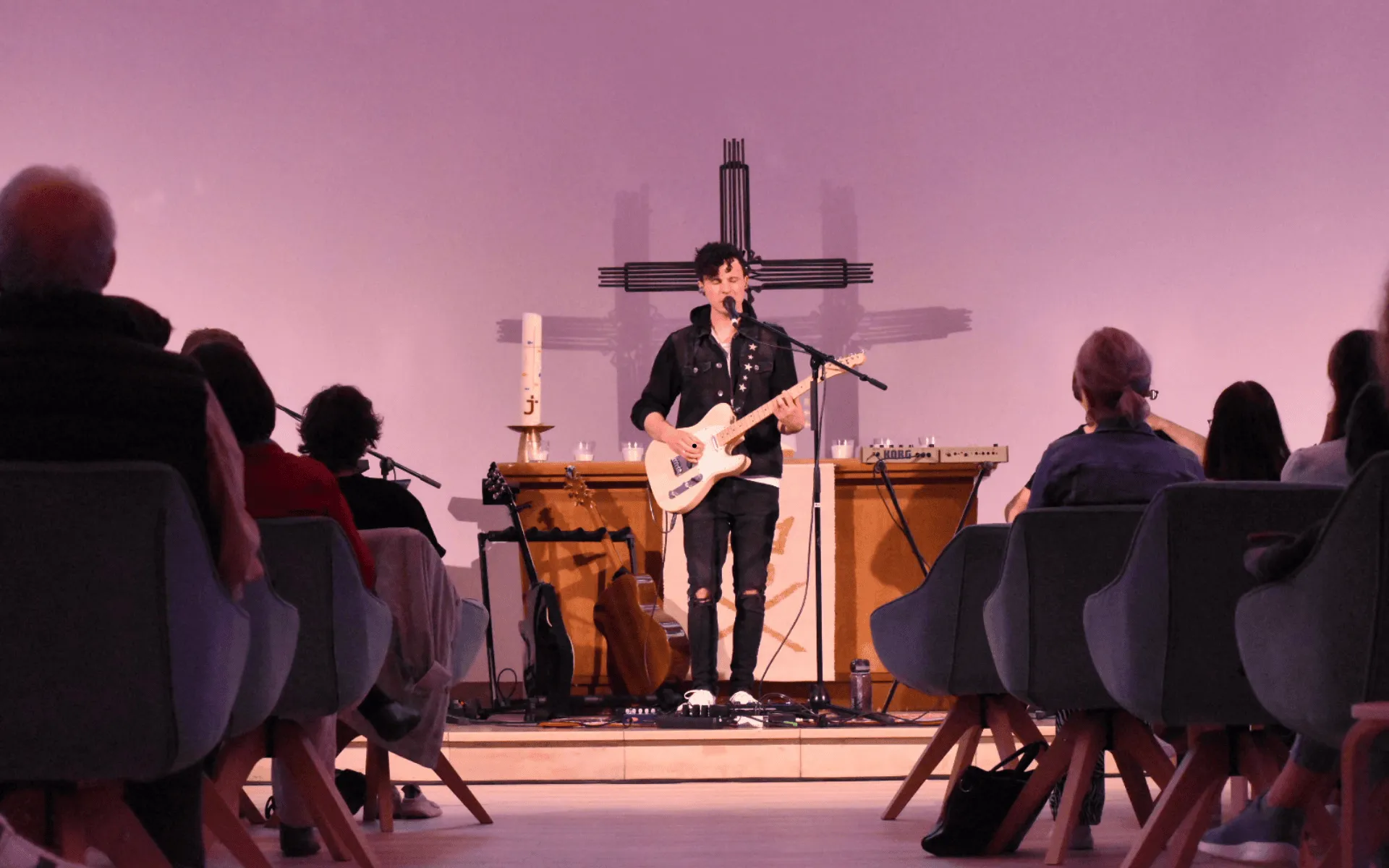 Man sieht ein Foto eines Konzertes in der Jungen Kirche Gießen. Bastian Benoa singt und spielt Gitarre. 