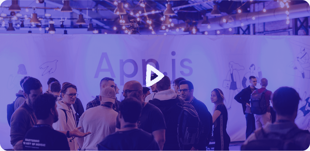 Video overlay photo with play icon. Photo shows people in the venue attending the conference, talking and eating.