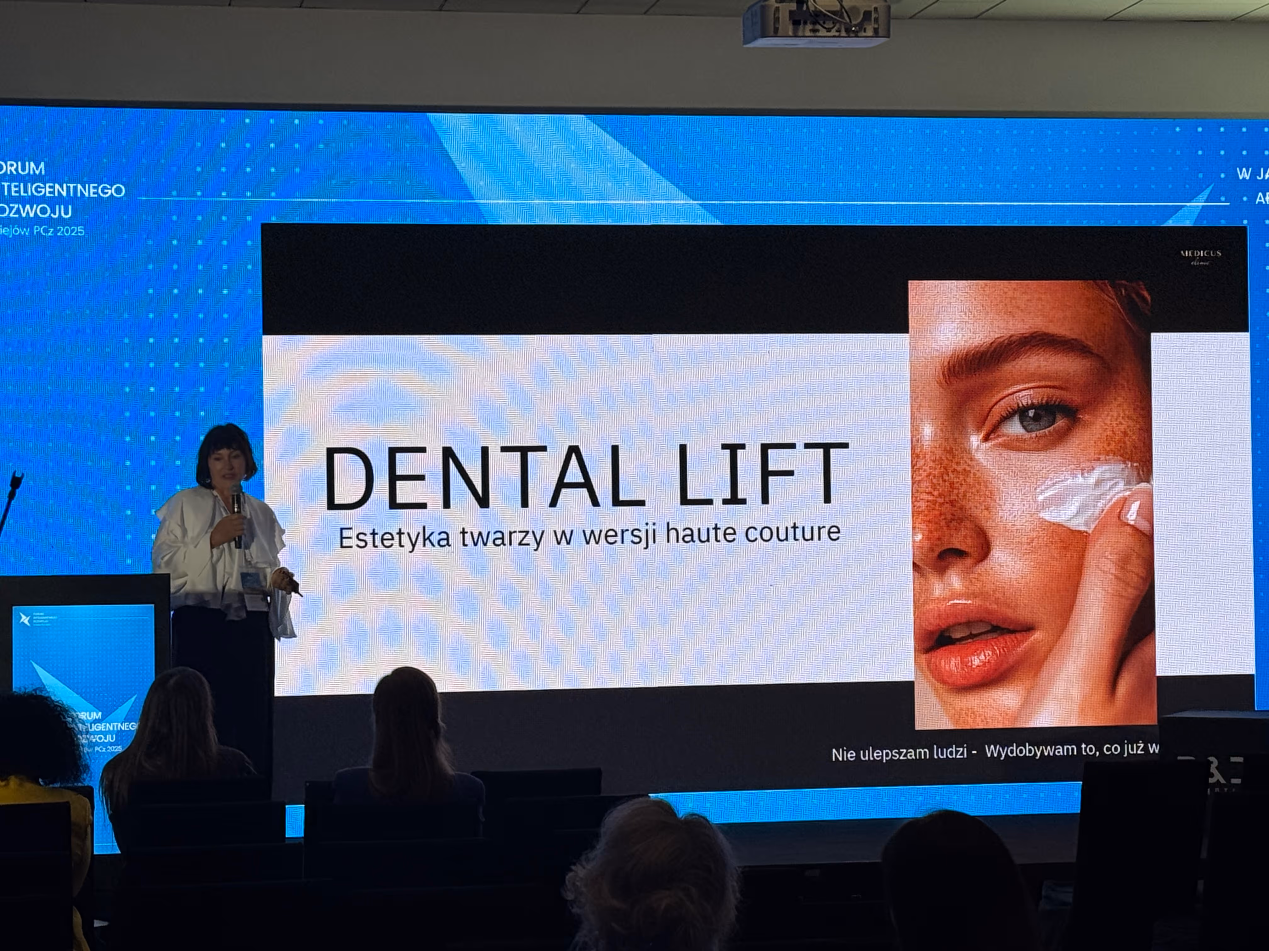 Ewa Abramowicz  prowadzi prezentację na konferencji, stojąc obok slajdu z tytułem „DENTAL LIFT – Estetyka twarzy w wersji haute couture”, na tle dużego ekranu z grafiką kobiecej twarzy.