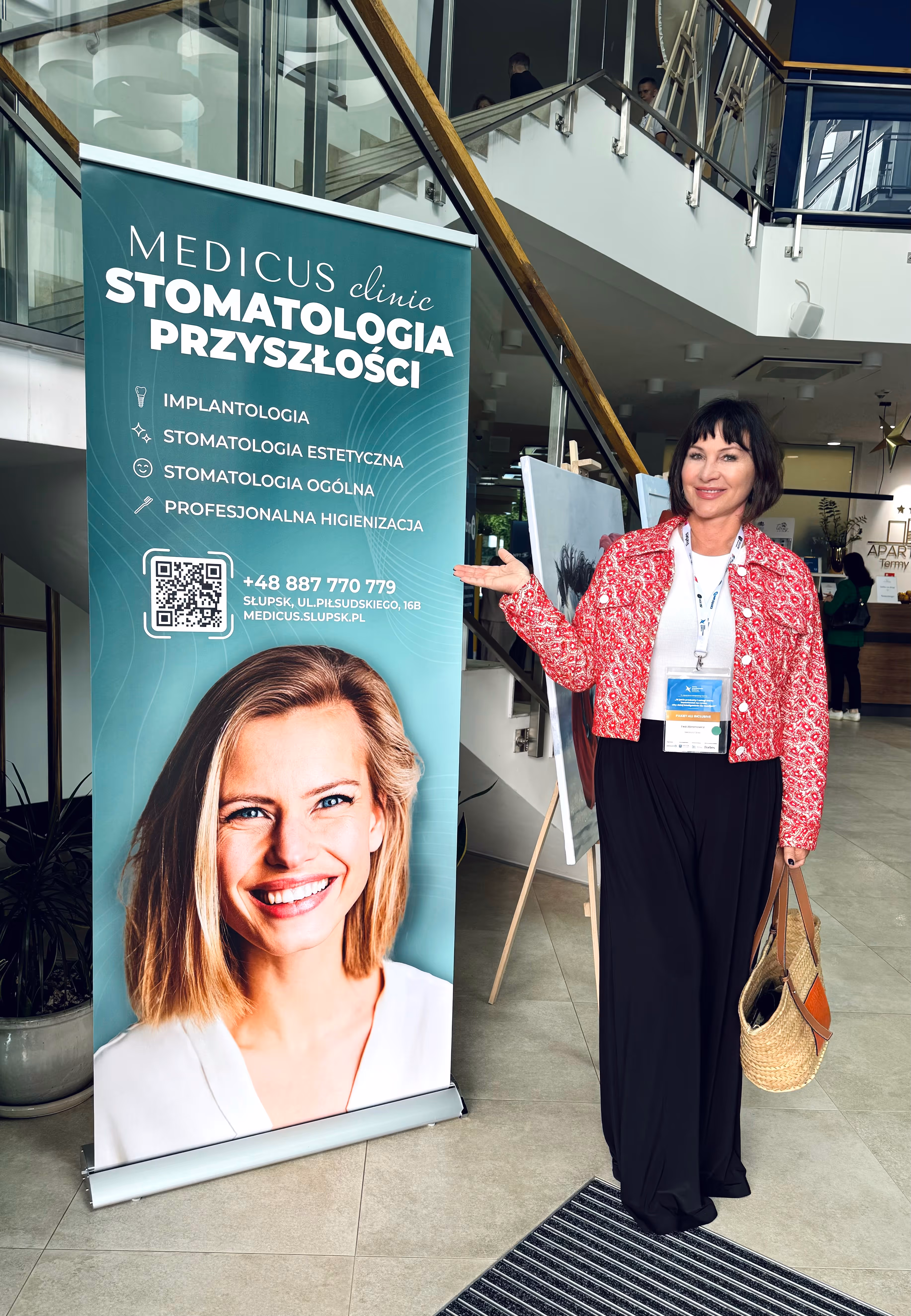 Ewa Abramowicz stojąca i wskazująca na znajdujący się obok banner promujący medicus clinic