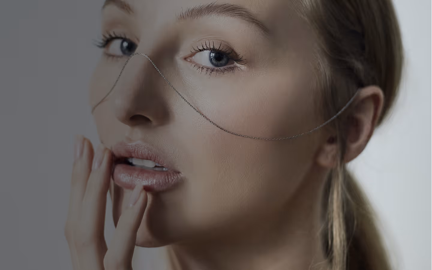 Zbliżenie twarzy młodej kobiety z jasnymi oczami i delikatną łańcuszką przechodzącą przez nos.