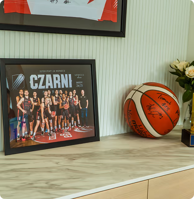 Zdjęcie grupowe drużyny koszykarskiej Czarni Medicus 2024/25 w czarnych strojach, obok podpisana piłka do koszykówki na jasnym blacie stołu.