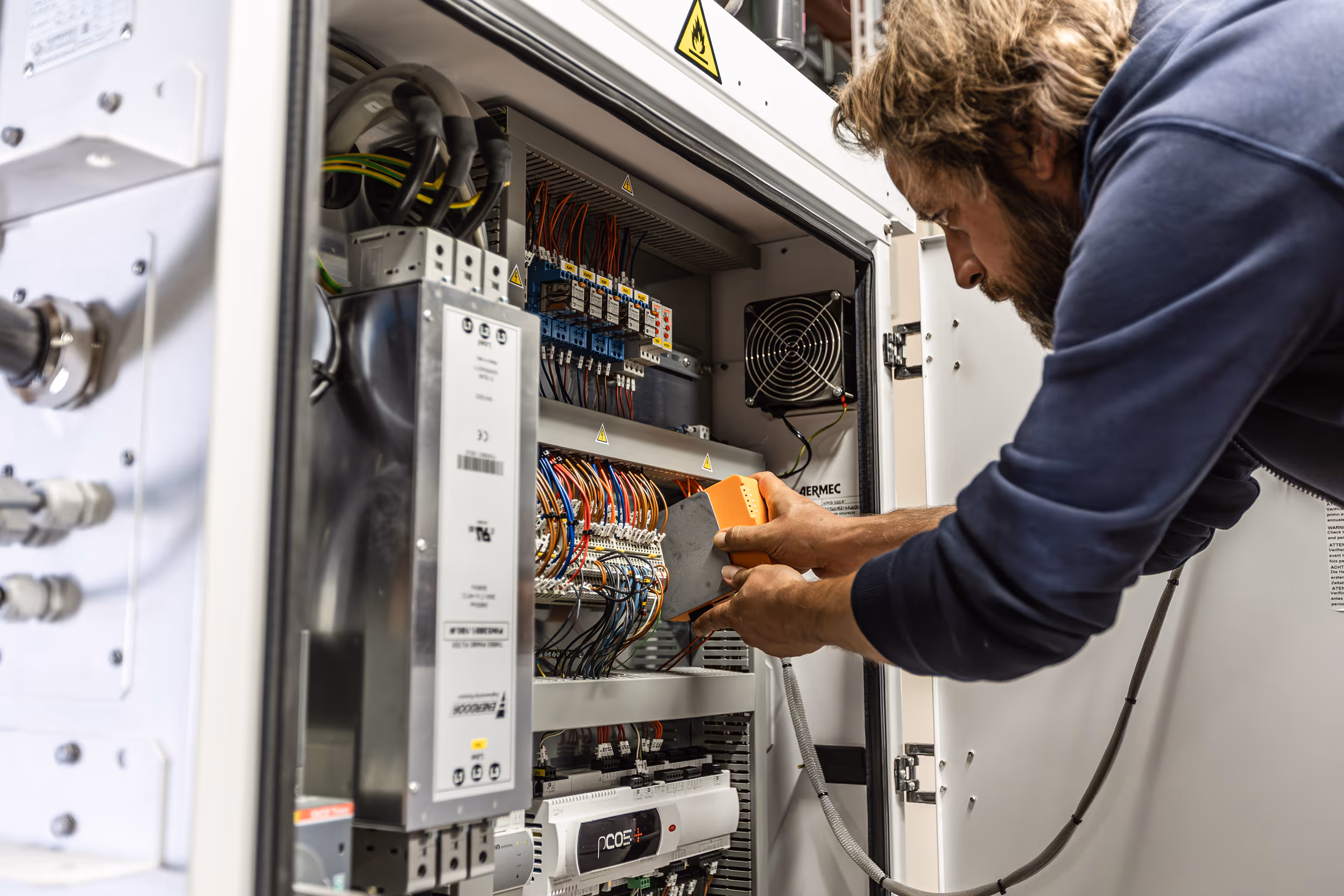 Technician working on electrical panel with wires and circuit boards.