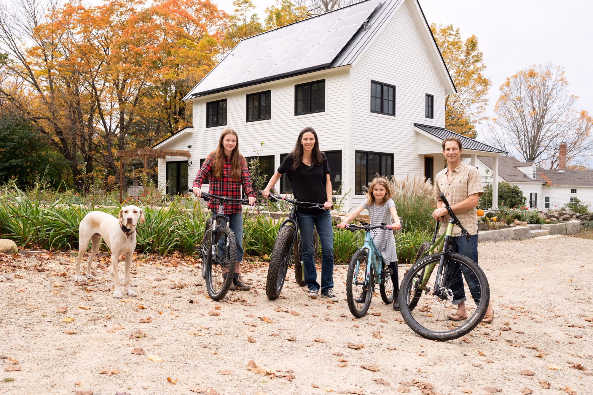 Family with bicycles and dog in front of white house during autumn
