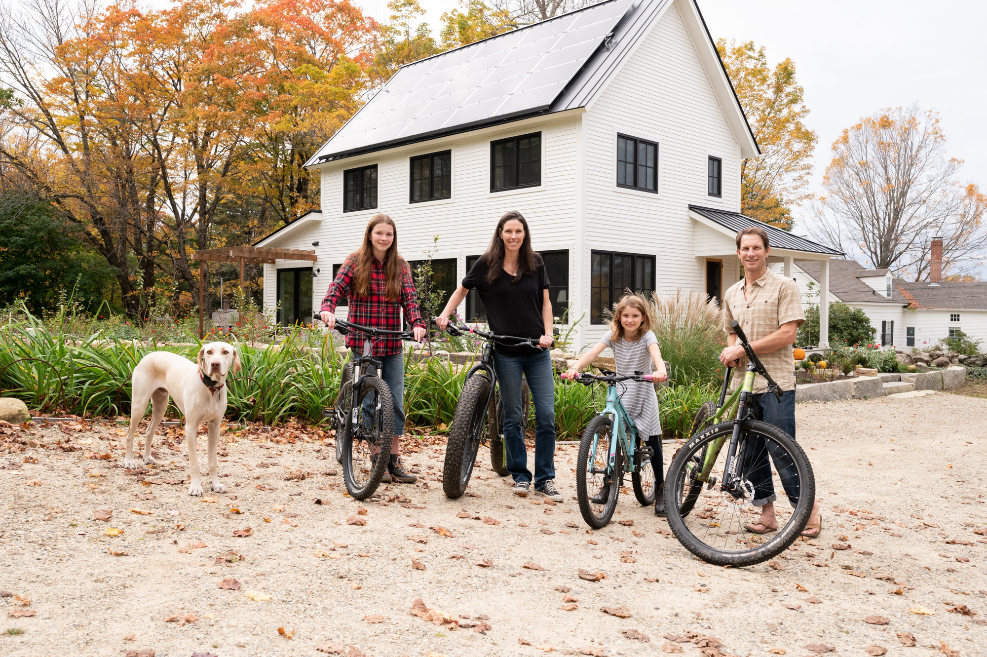 Family with bicycles and dog in front of white house during autumn